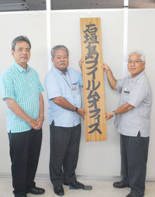 石垣島フィルムオフィスの看板を掲げる石垣市の大得観光文化スポーツ局長、市観光交流協会の高嶺会長、浦崎副会長(右から)=29日午後、同協会