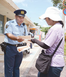 振り込め詐欺などの注意喚起のチラシを配布する警察官と受け取る市民=15日午後、八重山郵便局前