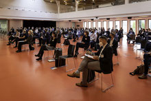 Der Blick in den Konferenzsaal mit den Teilnehmenden, die Stühle stehen den Corona-Vorschriften entsprechend mit einem Meter Abstand auseinander, die Teilehmenden tragen Mund-Nase-Bedeckung, einige machen sich Notizen