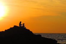 Deux silhouettes assises sur un rocher surplombant la mer à la tombée de la nuit