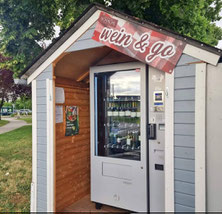 blaue Gartenhütte umfunktioniert zu Unterstand von Weinautomaten, Schild oberhalb der Türe mit der Aufschrift "Wein und Go"