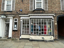 The shop front, the door on the left and the large shop window on the left. Shop items including clothes are displayed in the window.