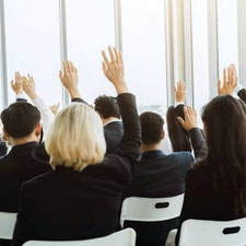 Schwarz gekleidete Menschen in einem Saal heben ihre Hand zur Abstimmung