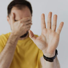 Ein Mann hält eine Hand vor die Augen, die andere abwehrend von sich gestreckt