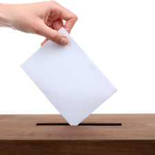Eine Hand wirft ein Kuvert in eine Wahlurne