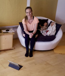 Hebamme Katharina Jeschke sitzt umgeben von Erste Hilfe Trainingspuppen auf einem Sessel und wartet auf die Teilnehmende des Erste Hilfe Kurses.