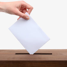 Eine Hand wirft ein Kuvert in eine Wahlurne