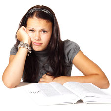 Ein Mädchen sitzt genervt über einem Schulbuch