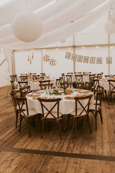 Crossbackstühle an einem Runden Tisch. Tisch mit weisser Tischdecke und schöner Dekoration auf einer Hochzeit in Kitzingen im Zelt.