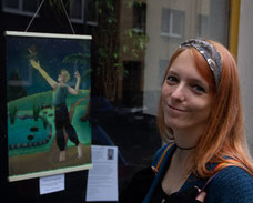 Foto der Autorin und Illustratorin "Megan E. Moll". Sie steht vor einem Schaufenster in dem eines ihrer Bilder ausgestellt ist.