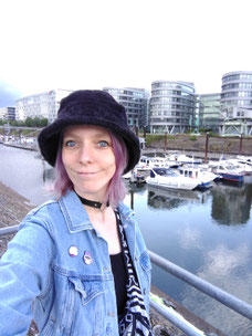 Foto der Autorin und Illustratorin "Megan E. Moll". Sie steht in einem Hafen, im Hintergrund sind Schiffe in einem Gewässer zu sehen. 