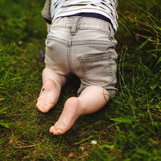 Hebamme Warendorf, Münster, Nordrhein-Westfalen, NRW Ein kleines Kind krabbelt im Gras. Es sind die Fußsohlen zu sehen.