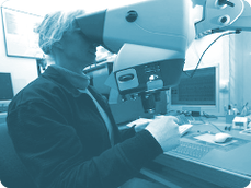Mitarbeiterin bei der Sichtkontrolle einer SMD Platine mit Stereo-Mikroskop
