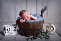 BabyfotografBaby liegt neben Wecker in einem Korb