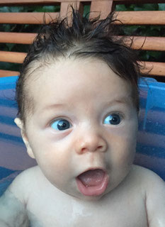 Ein neugieriges nasses Baby was in einen Wassertopf sitzt