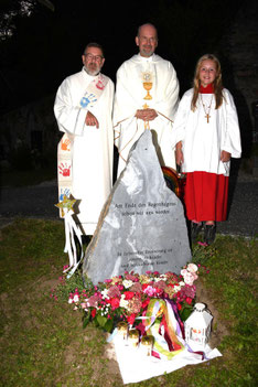 Beim Gedenkstein unweit des Friedhofskreuzes: Diakon Rupert Kremser, Moderator Oliver Becker und Ministrantin Valentina Meinhardt (v. l.).