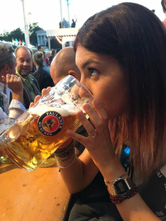 ragazza che beve un boccale di birra da un litro seduta ad una tavolata dell'oktoberfest di Monaco di Baviera