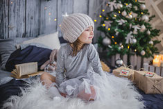 Content für Weihnachten, Kind mit Mütze auf Fell sitzend bewundert die Geschenkpakete