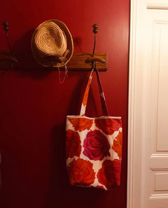 Tote bag en tissu à motif grosse fleurs roses et rouges sur porte manteau ancien