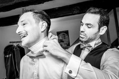 Un témoin aide le marié à ajuster son nœud papillon, partageant un moment complice et joyeux avant la cérémonie.