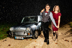 Reportage mariage Occitanie – moment spontané sous la pluie avec des invités devant une voiture vintage de nuit