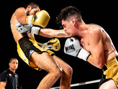 Un combat intense de boxe thaï capturé en plein impact : un boxeur en short jaune et gants dorés assène un coup de genou spectaculaire à son adversaire en short noir et or, qui tente de se protéger avec ses gants gris