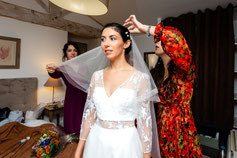 Photo prise par un photographe de mariage à Montauban montrant la mariée en robe blanche se prépare avec l'aide de ses proches, ajustant son voile dans une ambiance chaleureuse et émotive.
