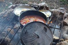 Beim Outdoorkochen köcheln die Speisen in den Kochtöpfen über dem Lagerfeuer – Abenteuer und Genuss für Gruppen