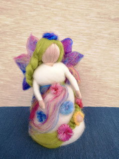Handgefilzte, bunte Fantasiefigur mit Flügeln, geflochtenem Haar und floralen Verzierungen auf hellem Hintergrund.