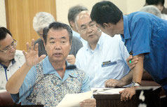 臨時議会の休憩中、議員の質問に答える川満町長=14日午後、議場