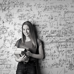 A girl with books stands in front of a whiteboard with equations