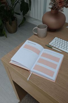 Foto: auf einem Tisch liegt ein aufgeschlagener Kalender, darüber ein Stift, Teil einer Tastatur ist zu sehe sowie ein Becher und eine Vase stehen dekorativ daneben 