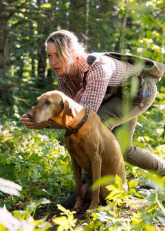 Jasna Behnke steht im Wald mit ihrer Vizsla Hündin und fokussiert den Hund auf den anstehende Arbeit des Apports