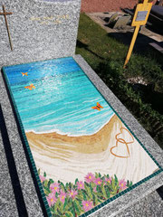 écoration de monument funéraire en mosaïque avec deux cœurs dessinés dans le sable et des vagues turquoise, création Mozaiktoone