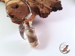 CH 9: Glasfläschchen gefüllt mit Haaren , ein wenig Asche und einem Flügelanhänger, angebracht ist ein Edelstahlring. Preis: 31 Euro