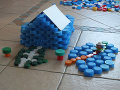 association de bouchons plastiques de différentes couleurs pour former un dessin en 3D (ici une maison et son jardin)