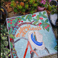 Mosaïque funéraire carrée et colorée portant l'inscription Mélanie Hélaudais, illustrant un chapeau de paille sur un guidon de vélo entouré de fleurs de cerisier