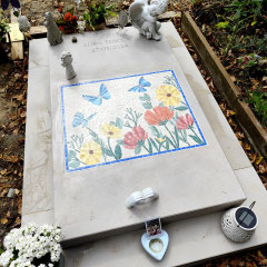 Monument funéraire blanc orné d'une plaque en mosaïque colorée et de petites statues d'anges.