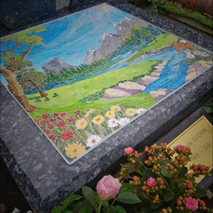 "Détail d'une mosaïque contemporaine représentant un paysage alpin, sommets enneigés, sapins et prairies fleuries, art funéraire personnalisé."