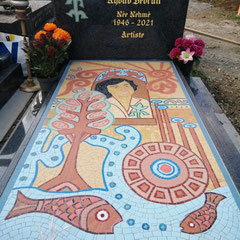 Vue d'ensemble d'une œuvre en mosaïque colorée posée sur une tombale en granit, dans un cimetière.