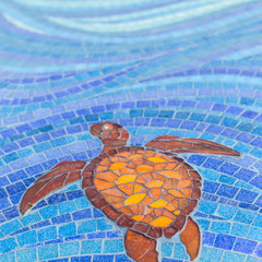 Gros plan sur les détails d'une tortue de mer réalisée en mosaïque avec des tesselles dans les tons marron, orange et jaune, contrastant avec le fond de vagues bleues.