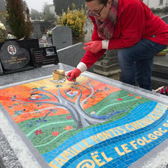 Artiste mosaïste en train de réaliser les joints d'une grande mosaïque colorée sur un monument funéraire au cimetière.