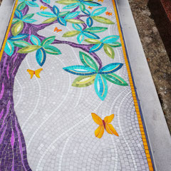 Détail d'une mosaïque représentant un arbre de vie avec un  tronc aux nuances de violet et mauve, des feuilles turquoise et des papillons jaunes et dorés.