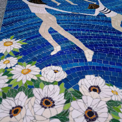 Détail d'un monument funéraire en mosaïque montrant des personnages stylisés en mouvement et une couronne de fleurs blanches sur fond bleu azur