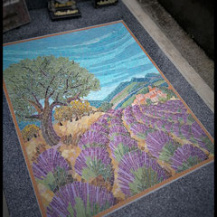 Gros plan sur les détails d'une mosaïque artisanale montrant les nuances de violet des brins de lavande et le tronc d'un olivier.