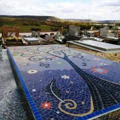 Artiste mosaïste dans son atelier en plein travail de création minutieuse d'une œuvre funéraire personnalisée pour une sépulture.