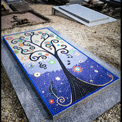 Monument funéraire recouvert d'une mosaïque contemporaine représentant un arbre de vie sur fond bleu azur et bleu nuit.