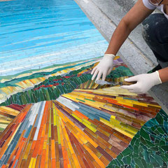 Gros plan sur les mains de l'artiste mosaïste Toone Nicol ajustant les tesselles d'un paysage coloré lors de l'installation au cimetière de Maurepas.