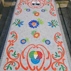 dalle funéraire entièrement ornée d'une mosaïque aux motifs floraux  sur fond gris et volutes colorés, rappelant les broderies traditionnelles.