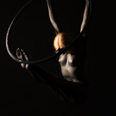 Performer Chiara Paradisi in posa su cerchio aereo (aerial hoop) con body painting nero su fondo nero - Fotografia di Alessandro Tintori
